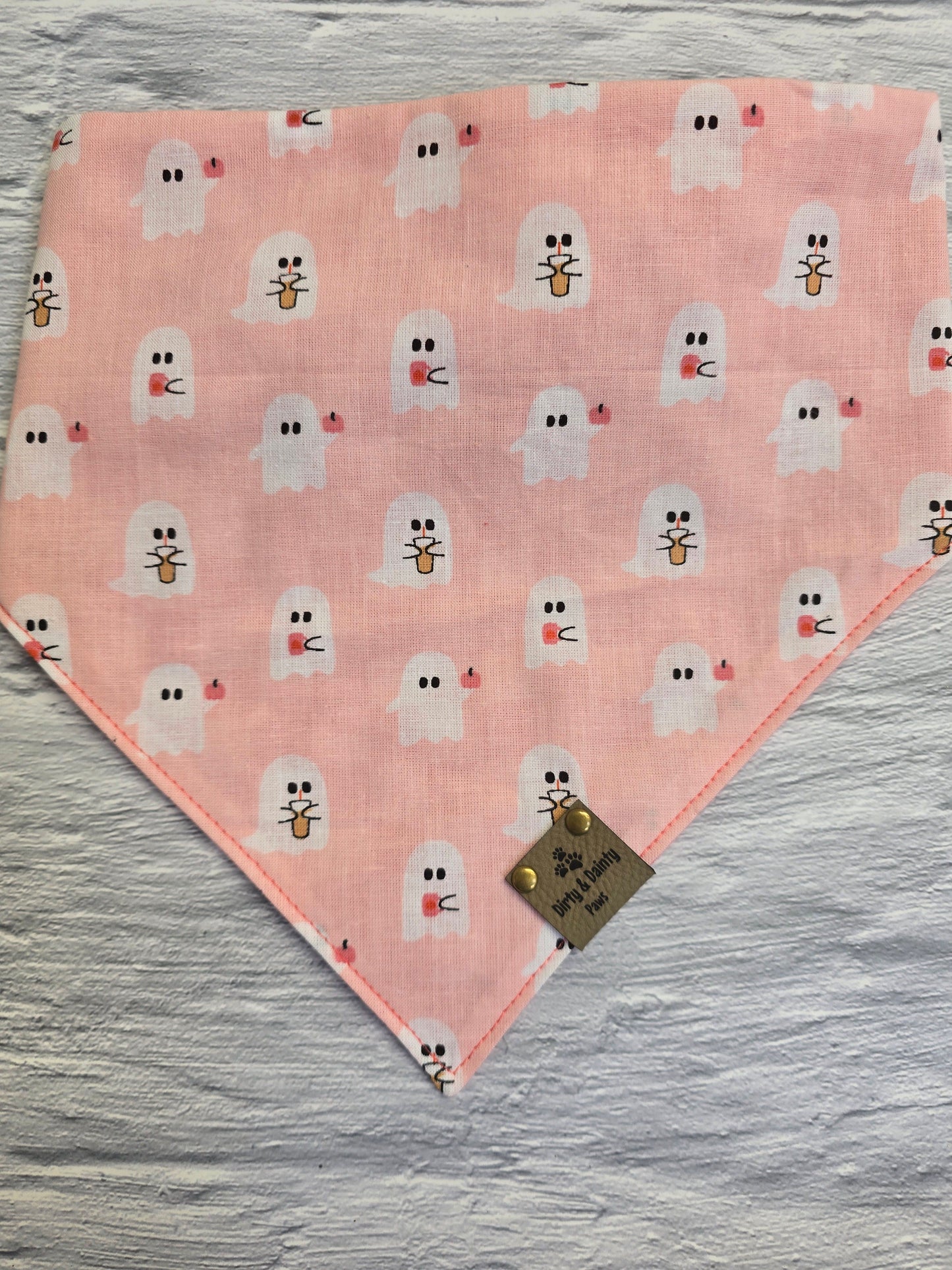 Reversible dog bandana featuring a cozy design of coffee cups and pumpkin ghosts on one side and a playful pink checkers pattern on the other, with a scrunchie-style collar perfect for adding charm to your dog's fall adventures.