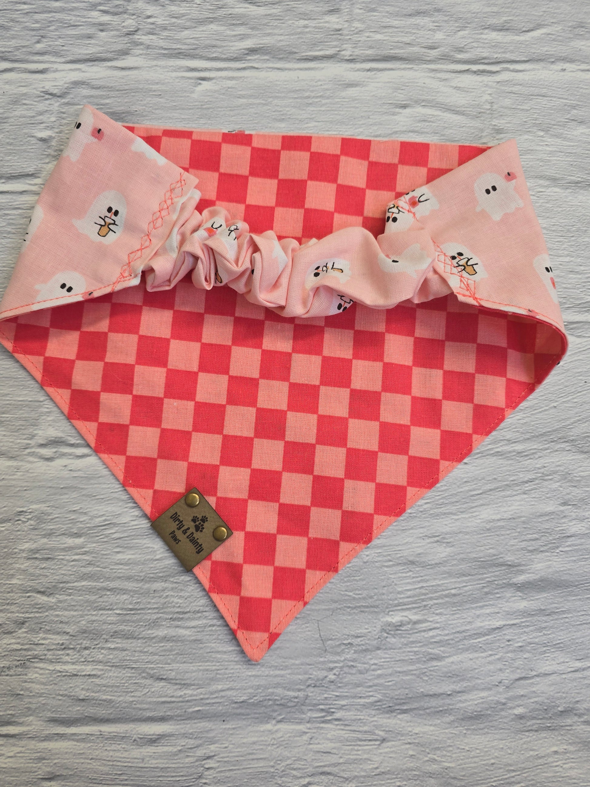 Reversible dog bandana featuring a cozy design of coffee cups and pumpkin ghosts on one side and a playful pink checkers pattern on the other, with a scrunchie-style collar perfect for adding charm to your dog's fall adventures.