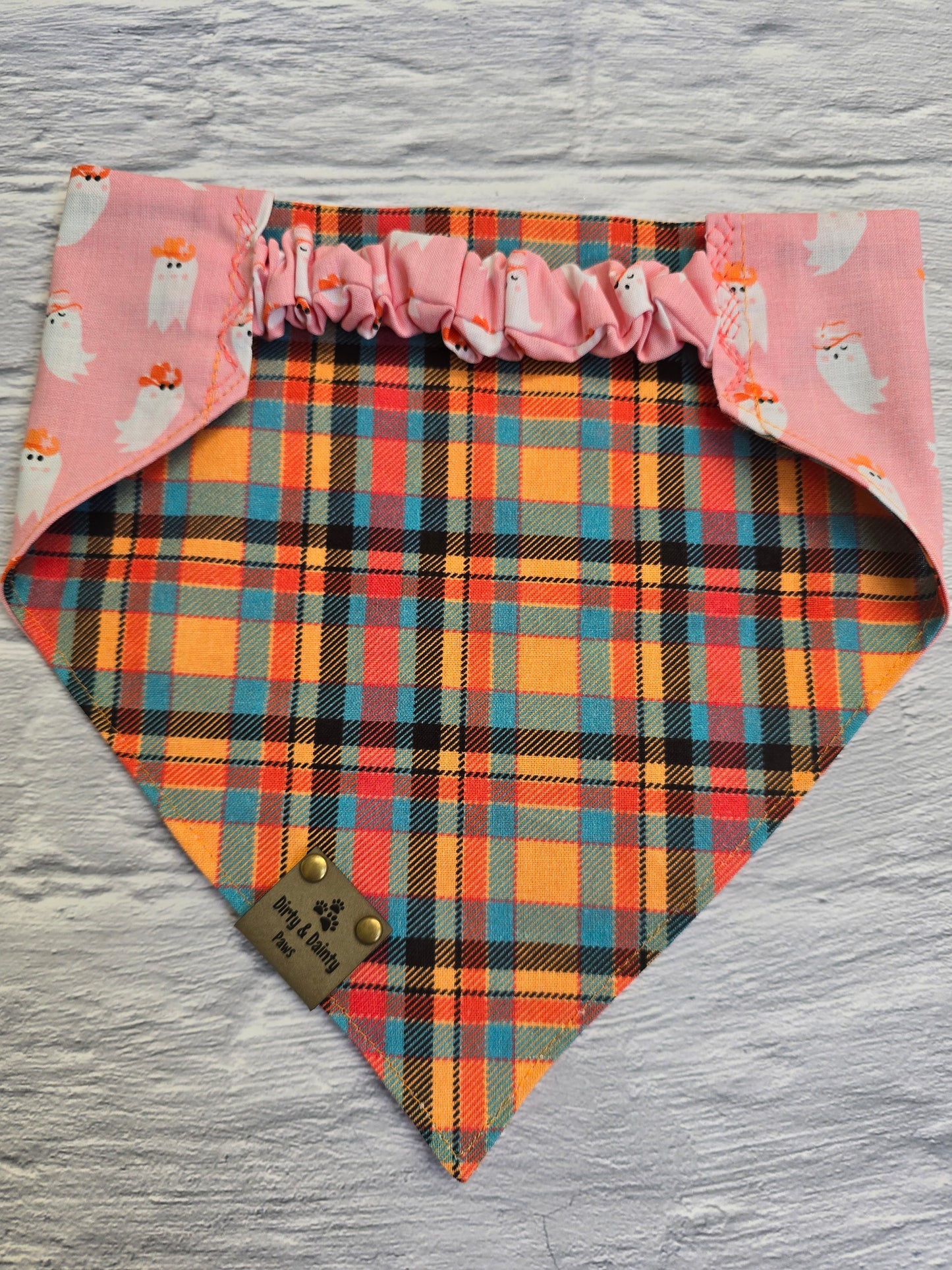 Reversible dog bandana featuring playful cowboy ghosts on one side and a classic fall plaid on the other, with a scrunchie-style collar perfect for adding a spooky Western touch to your dog's autumn look.