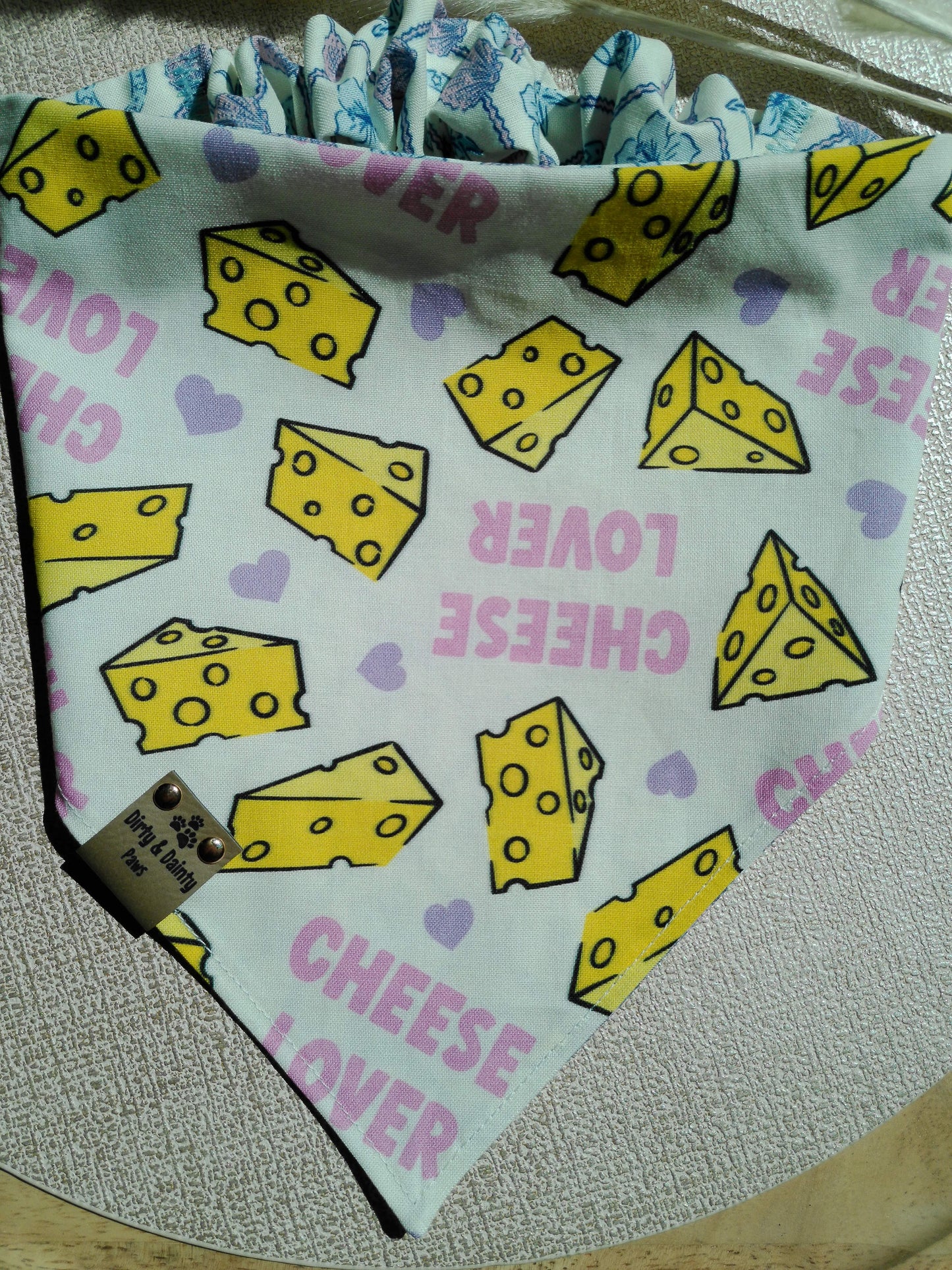 Reversible Cozy Cotton dog bandana featuring a pastel coastal cowgirl print with seashells, turtles, horseshoes, and cowboy hats on one side and a playful cheese lover print on the reverse. Handmade scrunchie bandana by Dirty and Dainty Paws