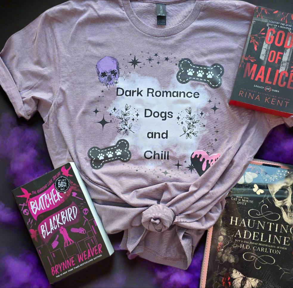 A soft mauve-colored t-shirt with the words "Dark Romance Dogs and Chill", featuring gothic-inspired designs like a skull, bones, and stars. Styled with dark romance books.