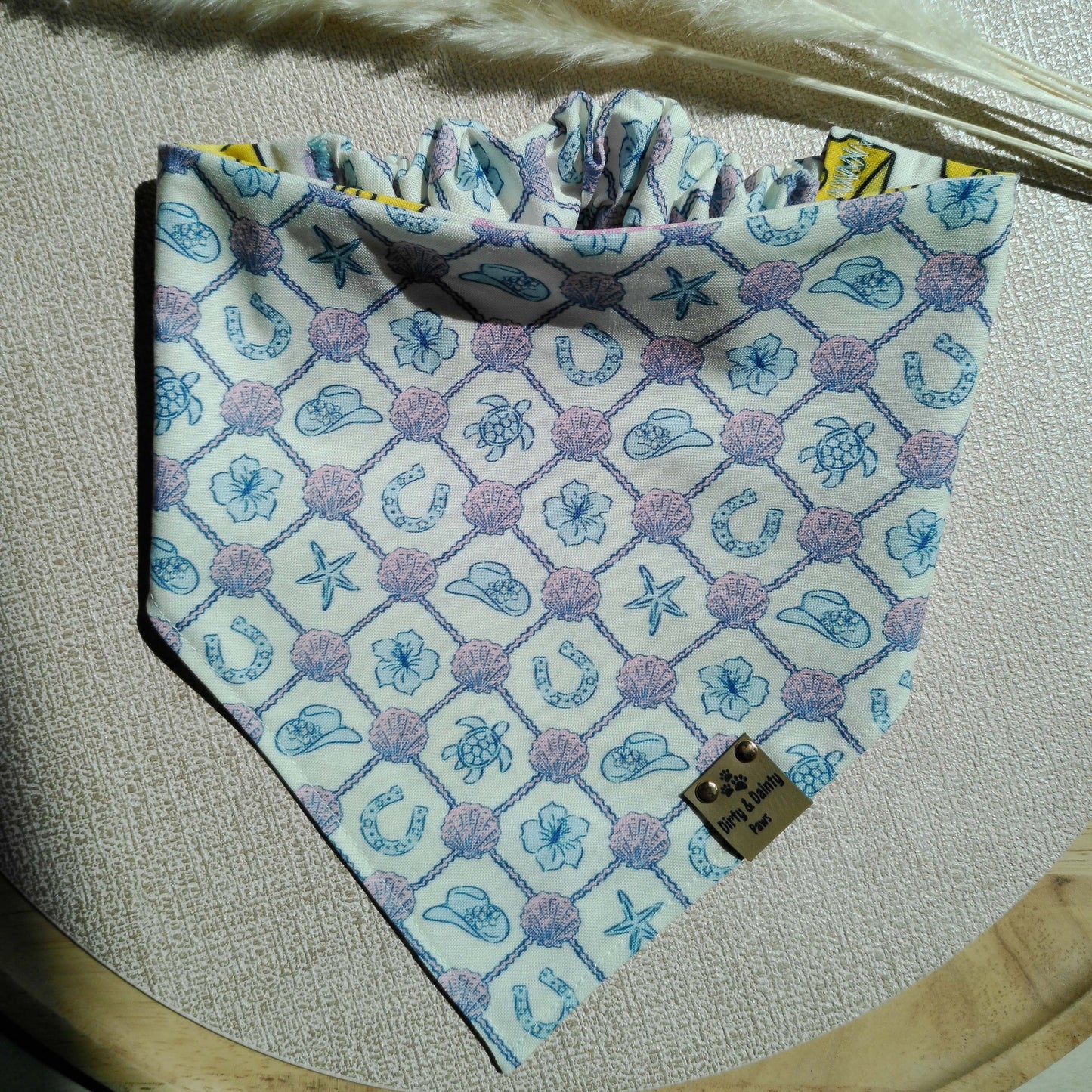 Reversible Cozy Cotton dog bandana featuring a pastel coastal cowgirl print with seashells, turtles, horseshoes, and cowboy hats on one side and a playful cheese lover print on the reverse. Handmade scrunchie bandana by Dirty and Dainty Paws