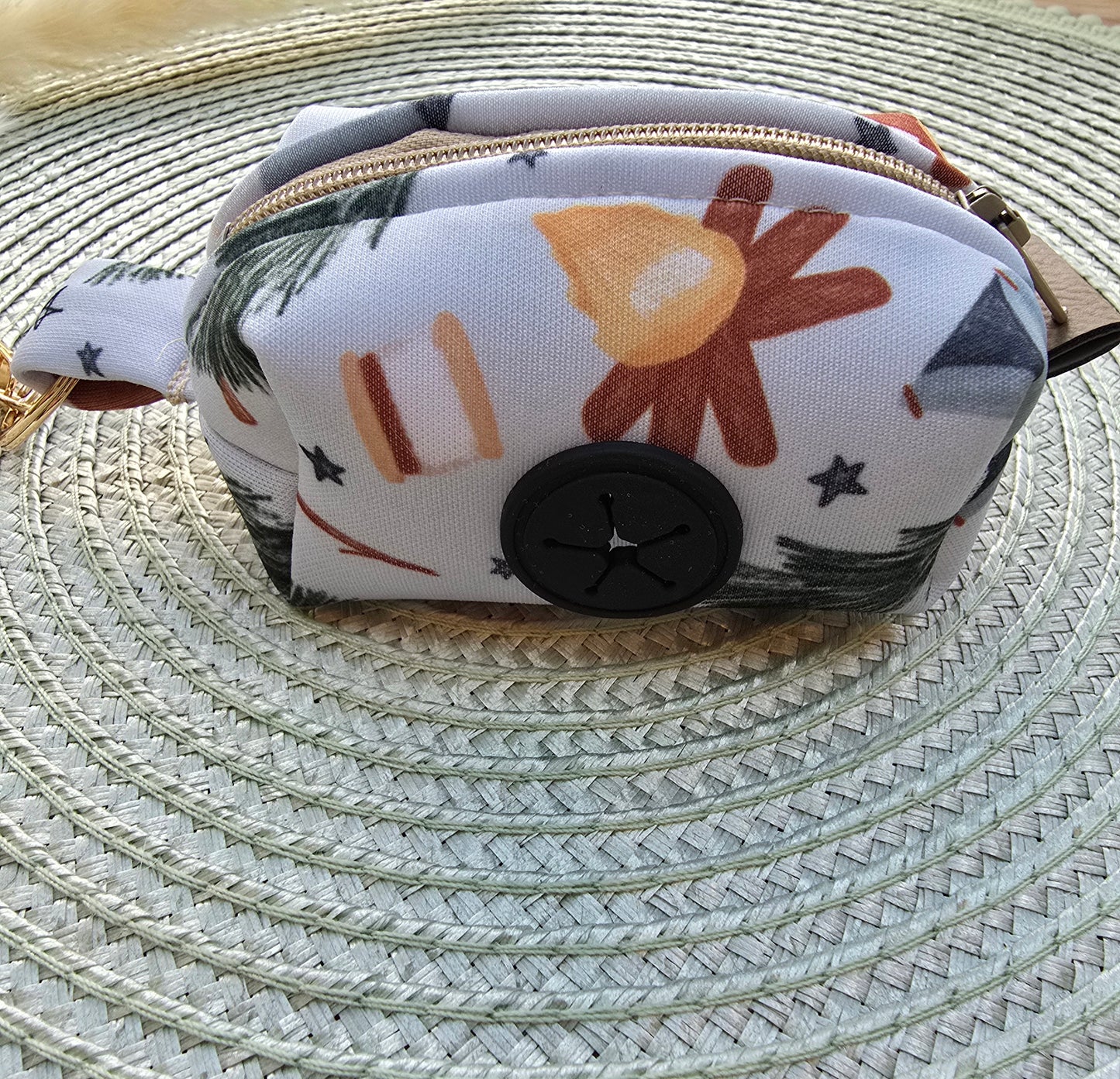 Watercolor camping print on a small waste bah holder made of neoprene with a small circular rubber black dispenser and an almond colored zipper