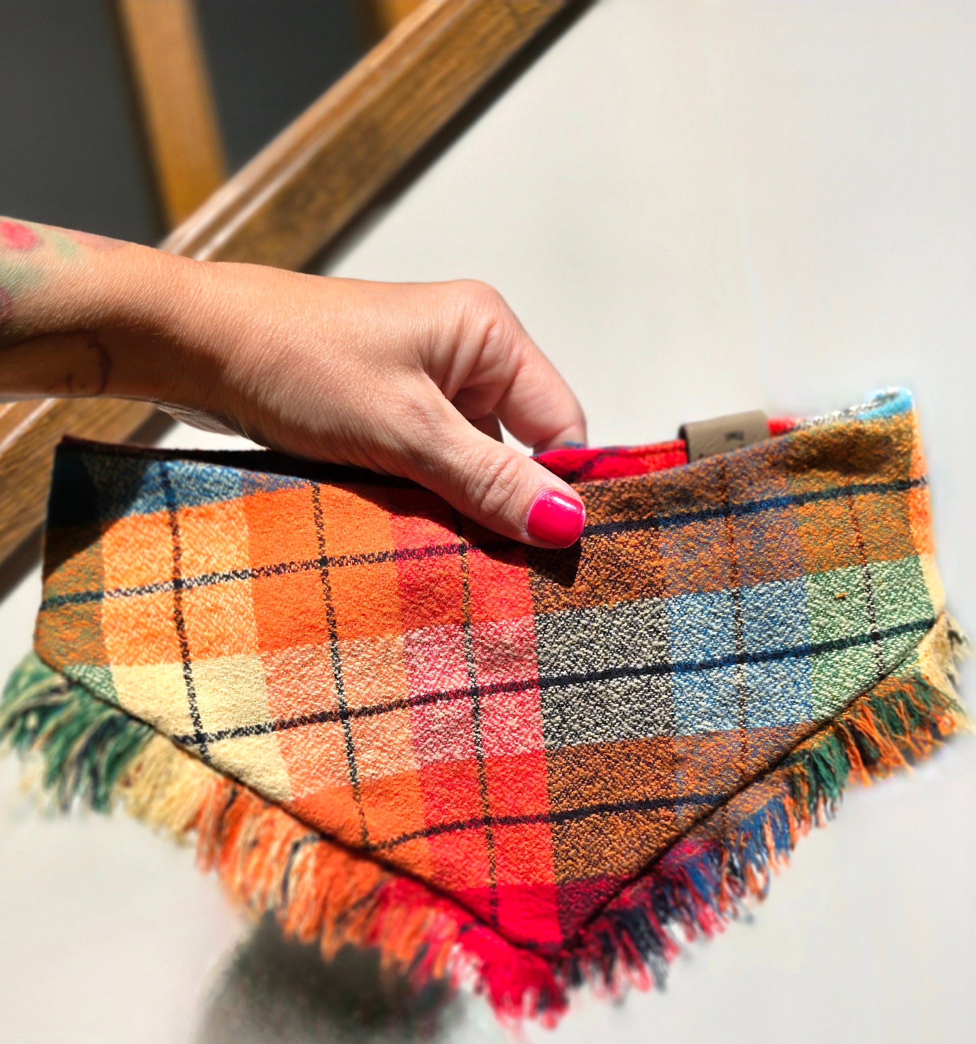 Colorful plaid dog bandana made from high-quality flannel, featuring hand-fringed edges, a secure snap closure, and a faux leather logo tag. Perfect for fall, the bandana showcases a vibrant mix of autumnal colors.