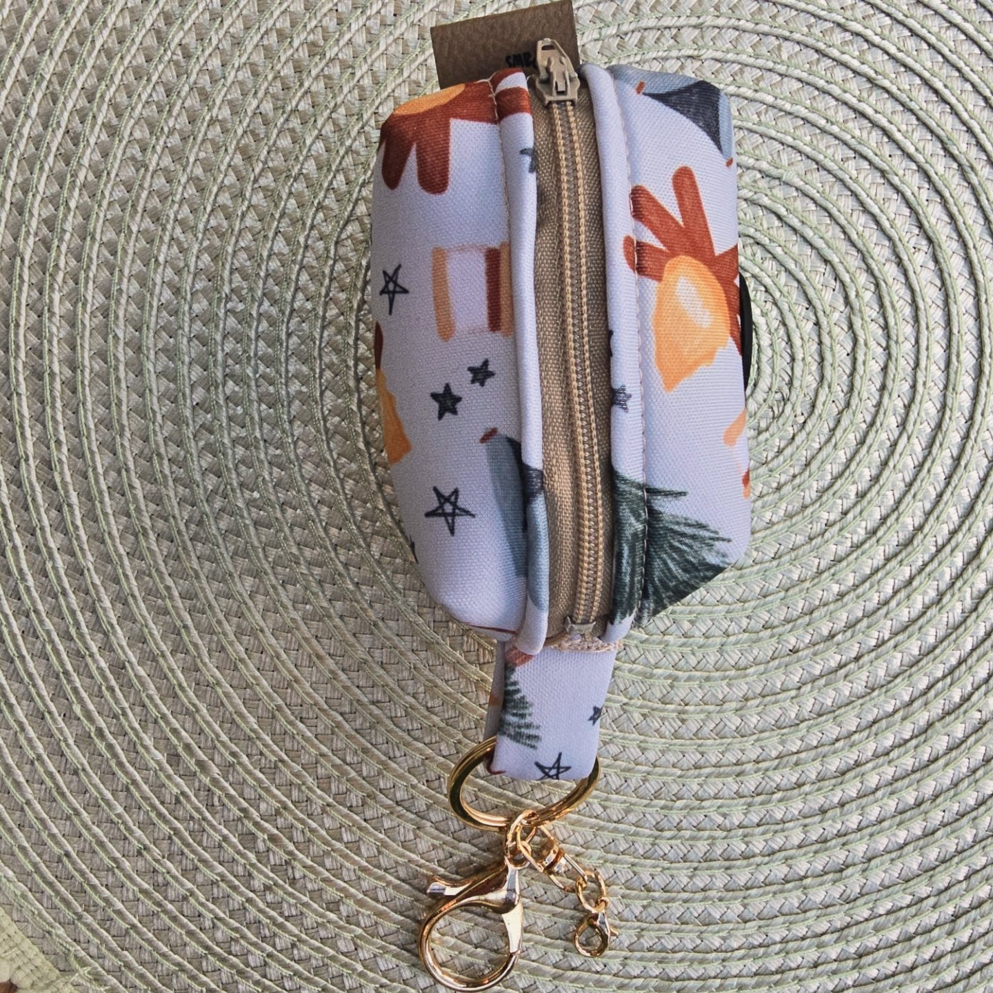 The top of the waste bag holder showing the almond colored zipper and also the yellow gold clasp which also has an extra clasp for a charm