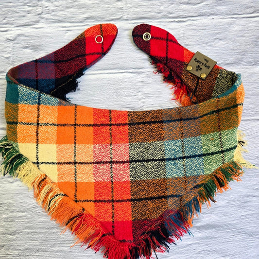 Colorful plaid dog bandana made from high-quality flannel, featuring hand-fringed edges, a secure snap closure, and a faux leather logo tag. Perfect for fall, the bandana showcases a vibrant mix of autumnal colors.