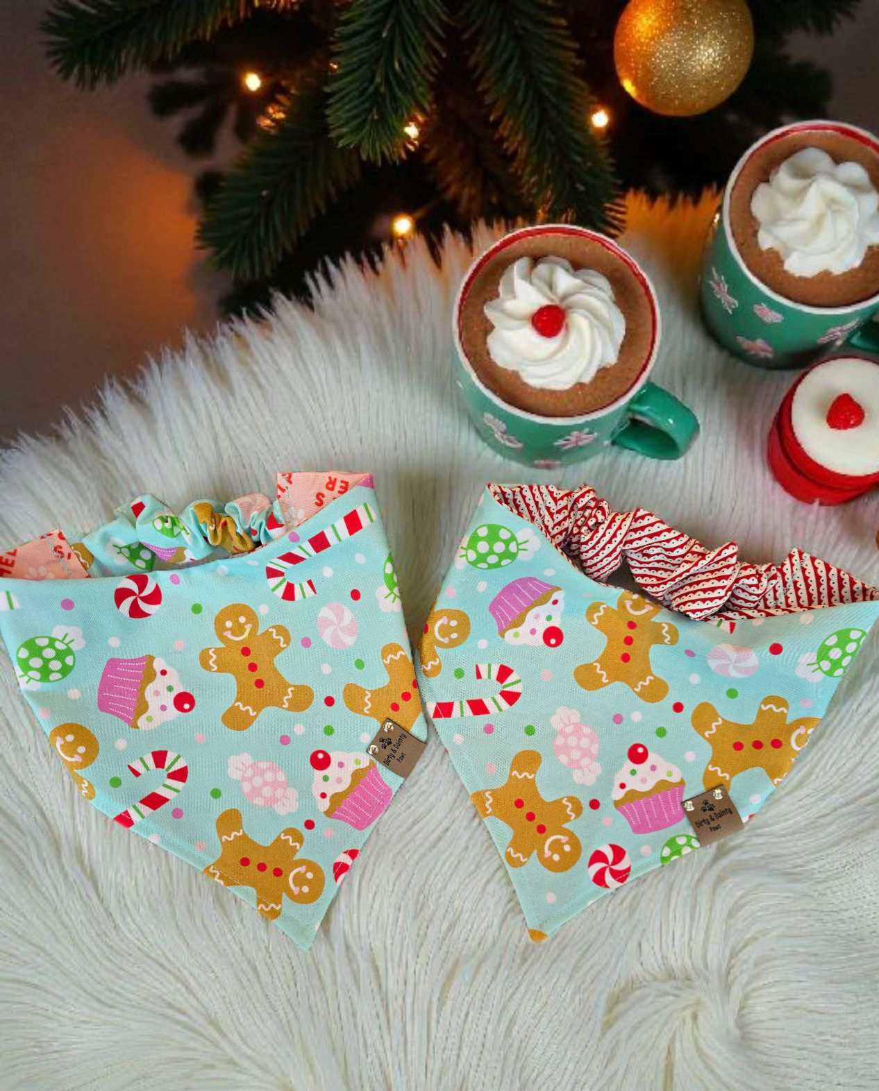 Two colorful dog bandanas with gingerbread and candy cane patterns on a fluffy white surface with hot chocolate and cookies.