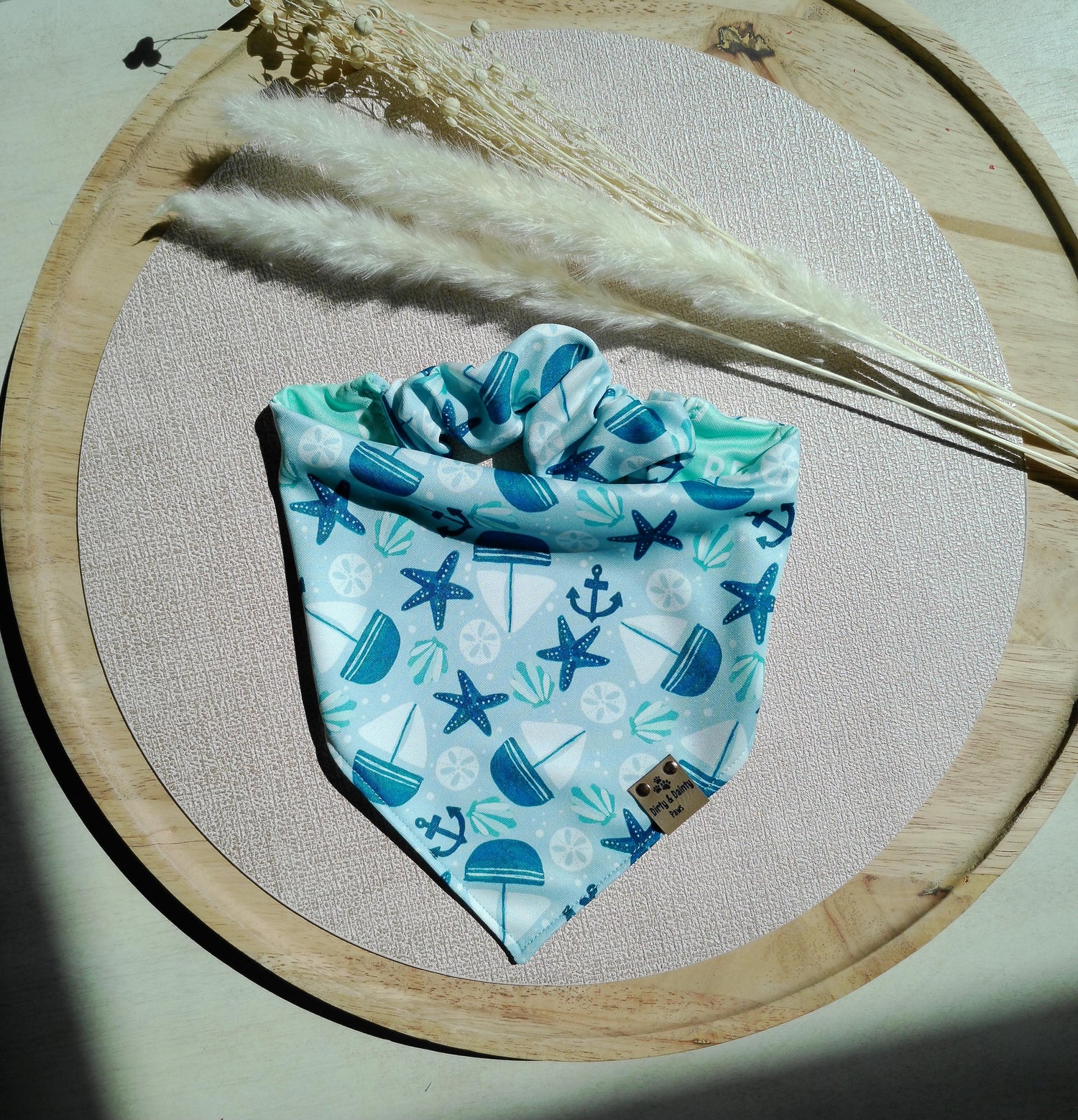 Reversible activewear dog bandana featuring a coastal beach print with sailboats, anchors, seashells, and starfish on one side and a mint “Beach Bum” palm tree print on the reverse. Handmade scrunchie dog bandana by Dirty and Dainty Paws