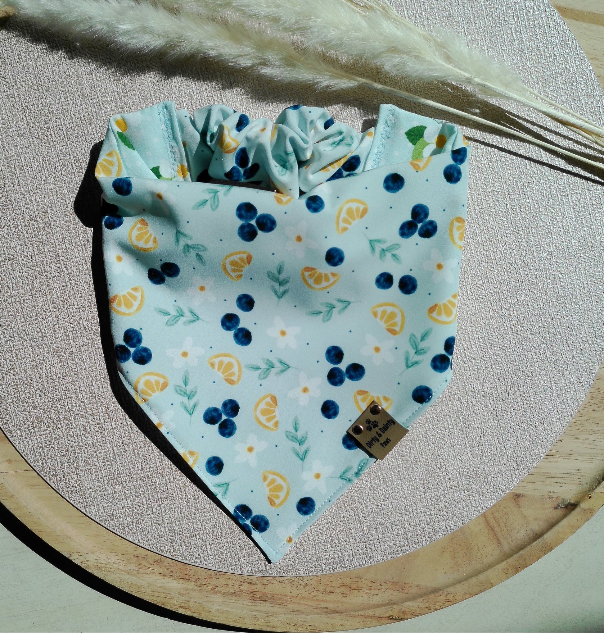Fabric bandana with blueberries and yellow flowers on a wooden board with dried plants.