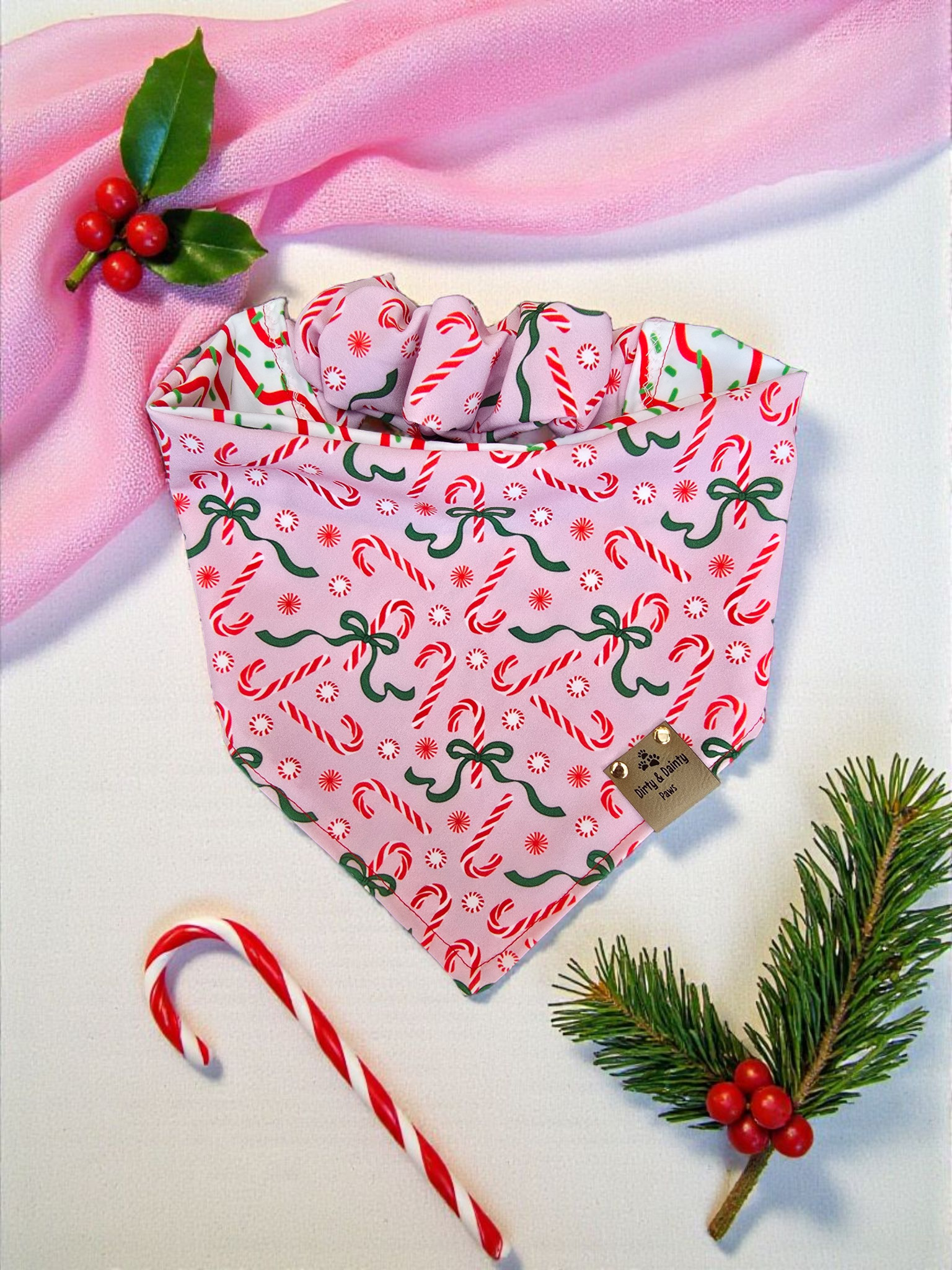 Christmas-themed dog bandana with candy cane and bow pattern on a pink fabric background.
